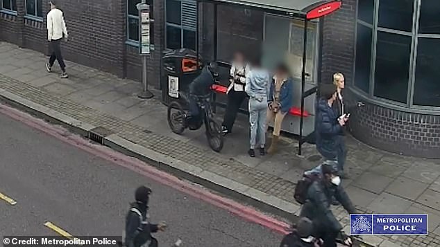 A masked gang riding e-bikes are seen here snatching a phone from a woman at a bus stop