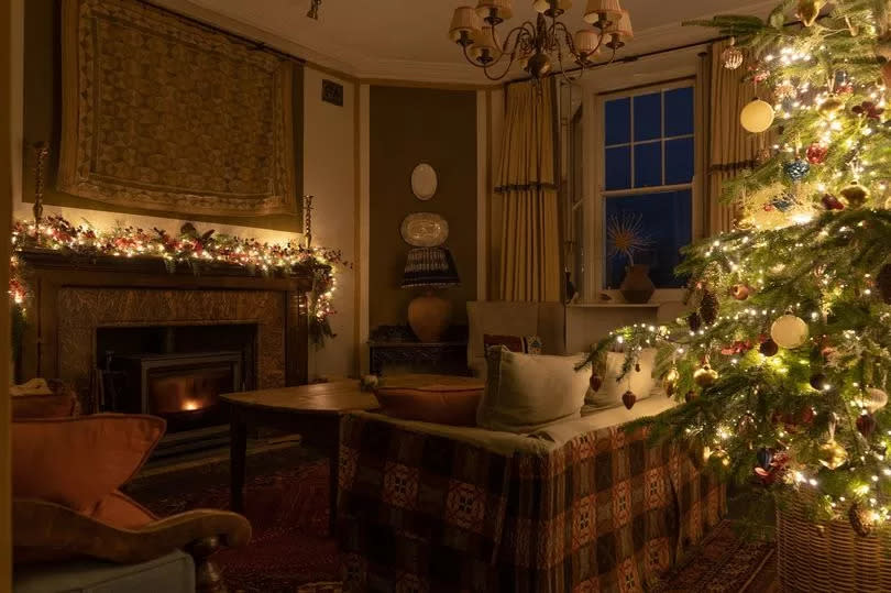 Cosy living room with a lit-up Christmas tree, sofas and an armchair in front of a log burning fire
