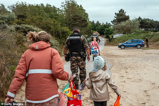 French gendarmes pass a family as they patrol a beach known to be used by people smugglers, on May 29, 2025 in Oye-Plage, France