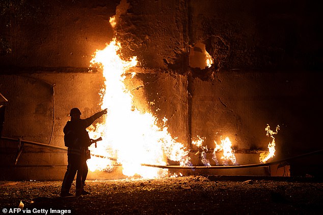 A firefighter stands by a fire and points to a hole following a drone strike in Kharkiv on June 5