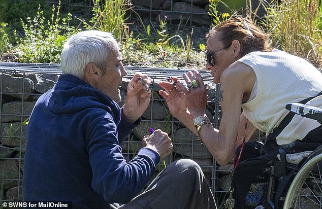 Two drug users, one in a wheel chair, hunch together as they light a crack pipe on a sunny day in Glasgow