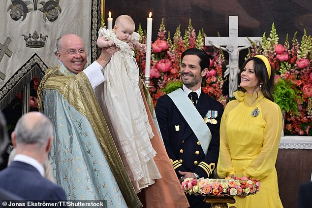 The chief priest, Bishop Johan Dalman, holds up Princess Ines after he baptizes her. Prince Carl Philip and Princess Sofia are pictured on the right