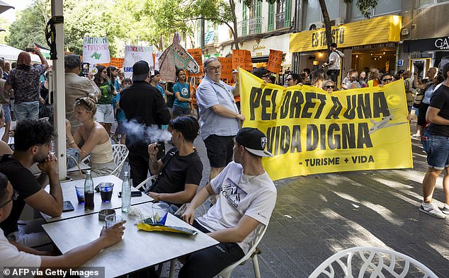 Tourists watch in Mallorca as demonstrators hold a banner reading 'For the right to a decent life' on June 15, 2025