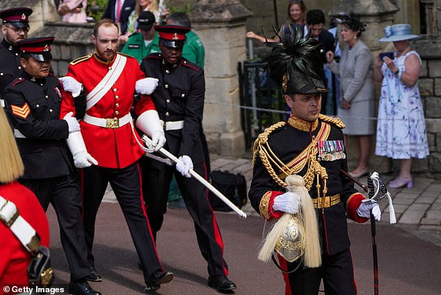 A member of the Household Cavalry has his helmet carried for him after he fainted, as attendees arrive for the Order of the Garter service at St George's Chapel, Windsor Castle