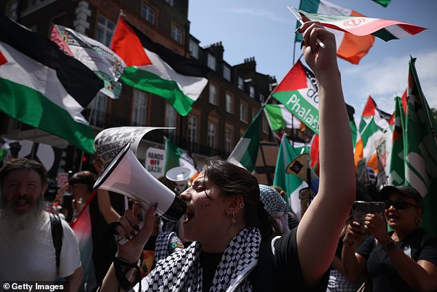 emonstrators hold Palestinian flags and placards and shout slogans