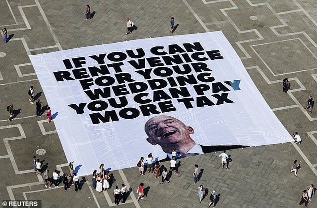 Amazon boss Jeff Bezos and bride to be Lauren Sanchez 's have been forced to change one of the venues for their £36million Venice wedding because of 'rising global tensions' it was claimed today. Pictured: A large banner against Amazon founder Jeff Bezos lies on the ground