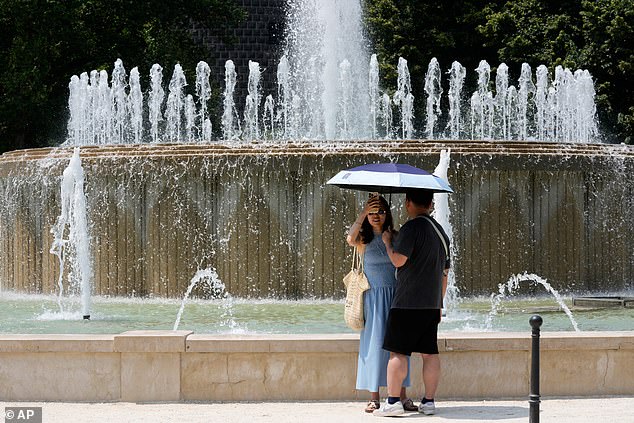 ITALY: Temperatures are also soaring over 40 degrees in Italy, the Balkans and Turkey. Pictured: Tourists shelter from the hot sun next to a fountain at the Sforzesco Castle in Milan on Friday