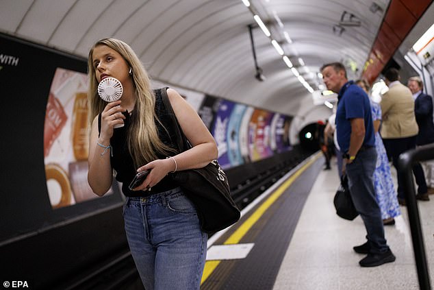 BRITAIN: A woman uses a portable electric fan to cool down on the London Underground public transport in London