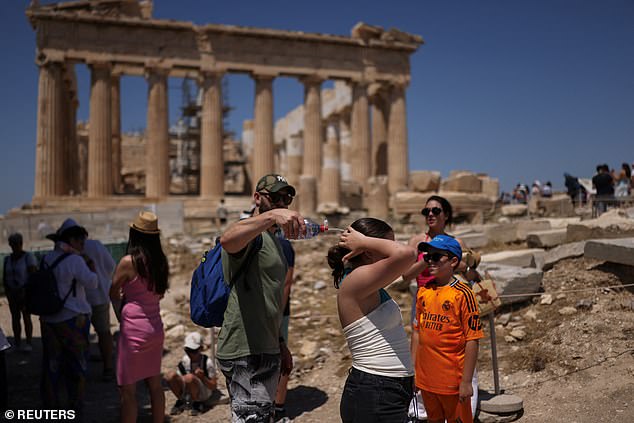 GREECE: A man tries to cool a girl with water during their visit to the Parthenon temple atop the Acropolis hill, as a heatwave hits Athens, Greece, June 27