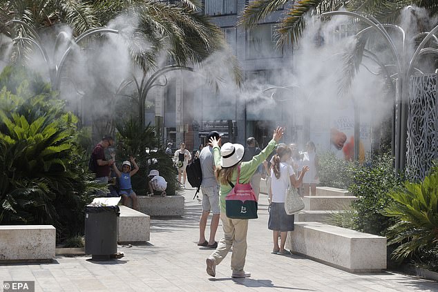 SPAIN -- Tourists cool off under a cloud of mist at the Plaza de la Reina during a heat wave in Valencia