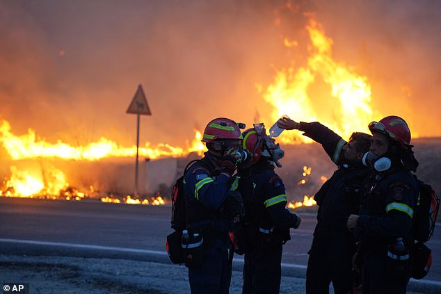 A firefighter pours water to cool down his colleague as they battle with a large wildfire burning on the Aegean island of Chios