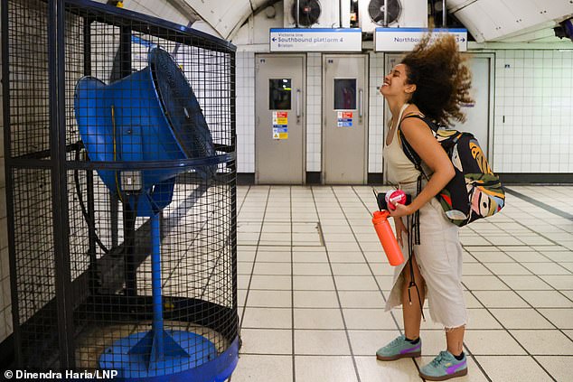A woman cools off in front of a large fan at a London Underground station