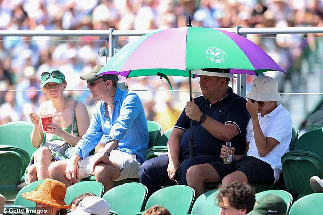 Spectators shelter from the sun under a Wimbledon Umbrella