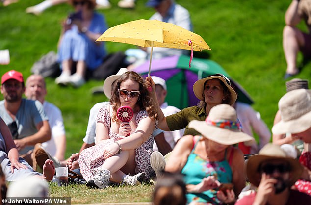 Spectators on the hill shelter with fans and umbrellas to shelter from the sun on day one of the 2025 Wimbledon Championships