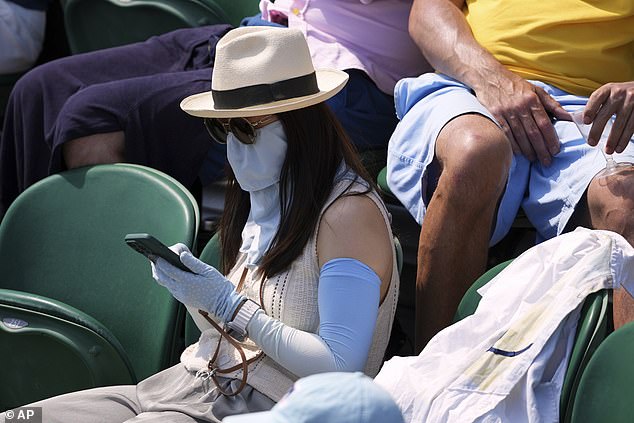 A woman protects her arms and face from the sun as she sits in the crowd