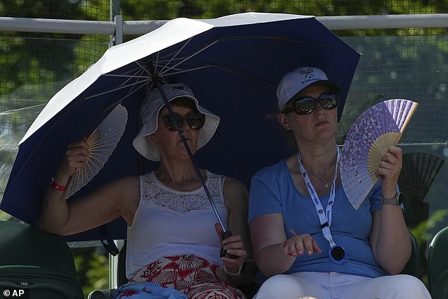 Spectators shelter from the sun under an umbrella