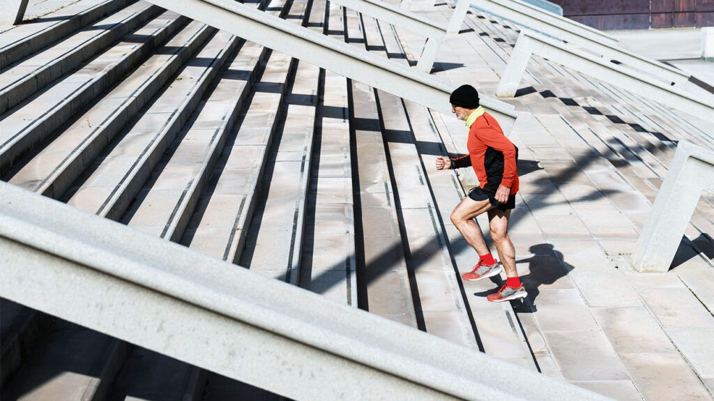 An older adult runs up stairs outside in running gear