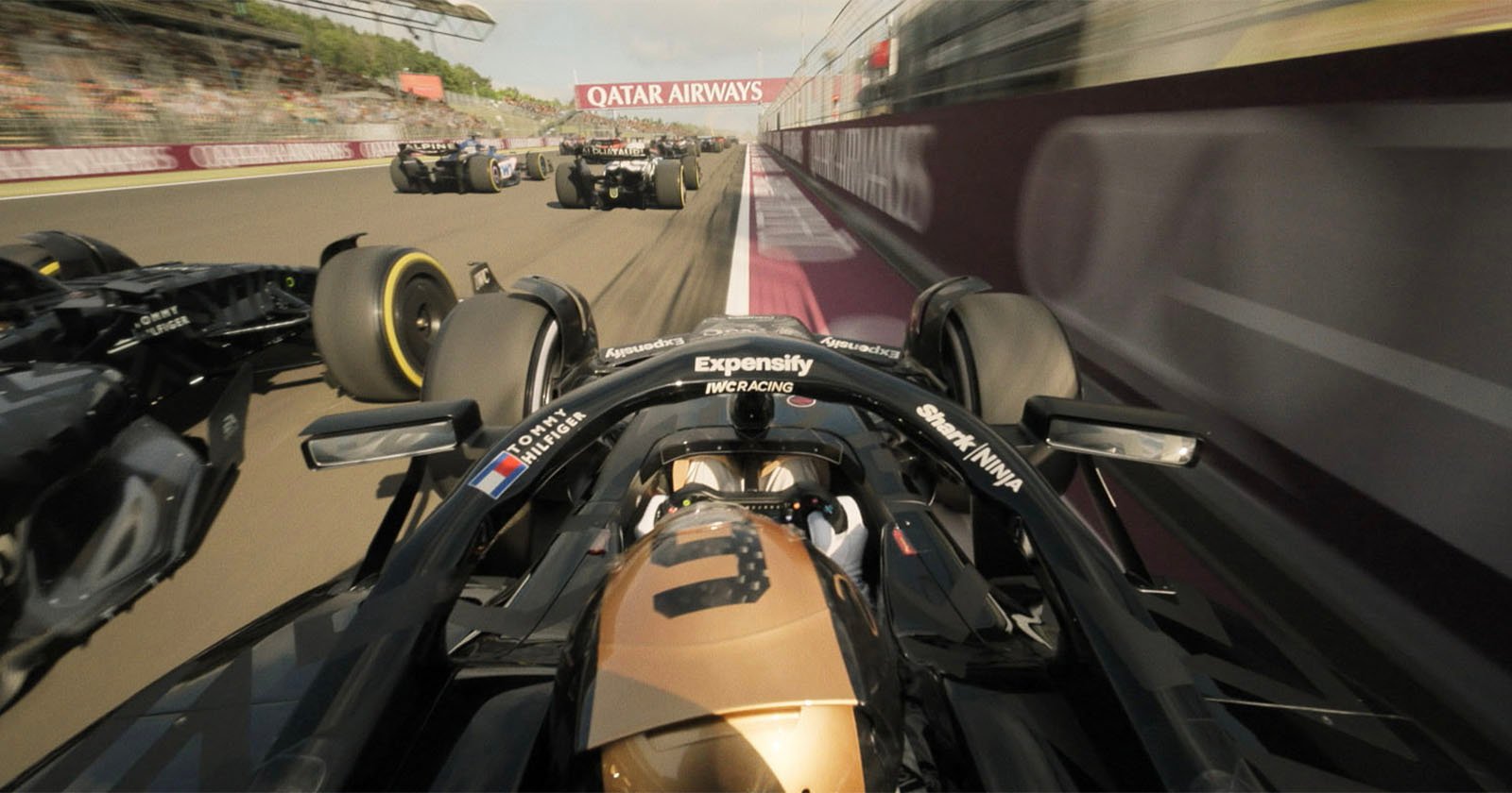 Onboard view from a black and gold Formula 1 car racing alongside several other cars on a track, with "Qatar Airways" banner visible above. The scene captures high speed and intense competition.