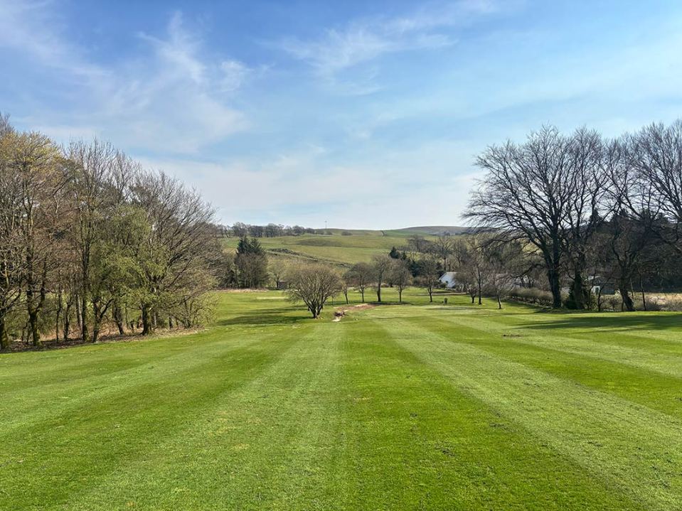 Golf course fairway with trees and hills in the background.