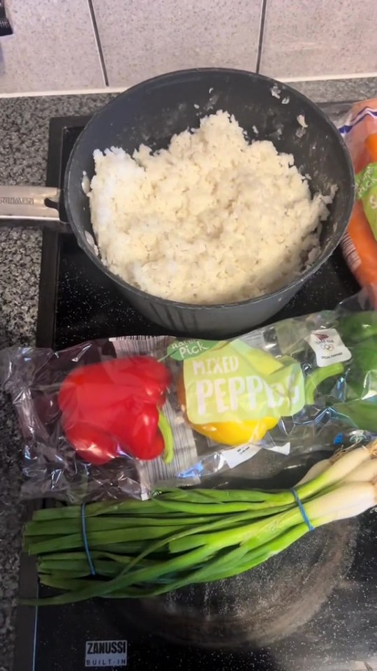 Cooked rice, bell peppers, and spring onions on a stovetop.