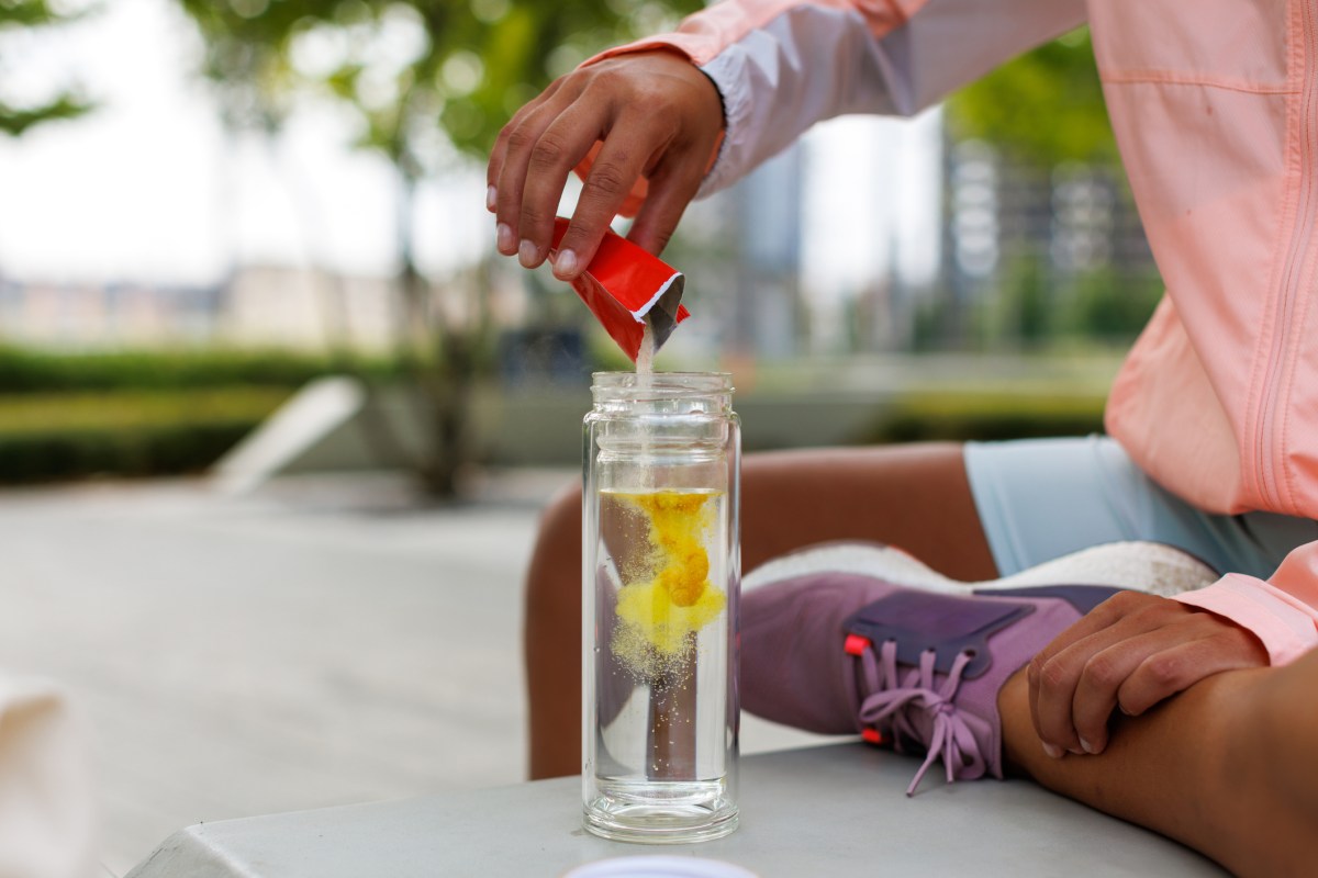 young woman in running gear pouring electrolyte powder into a clear bottle filled with water.