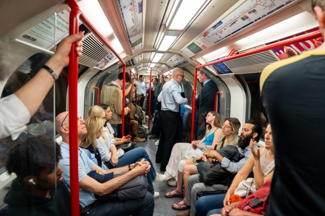Crowded Central Line Train Captures a Busy Rush Hour Scene with Commuters Holding Red Poles Amid Overhead Maps and City Energy.