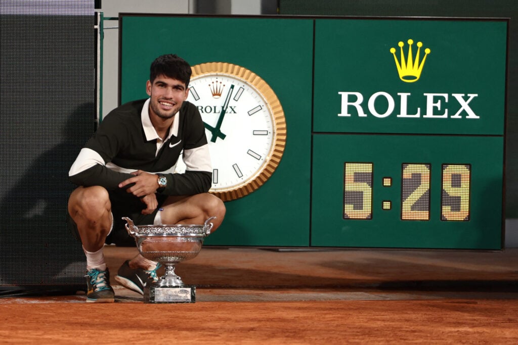 Carlos Alcaraz poses with the trophy next to the clock after the 2025 French Open final