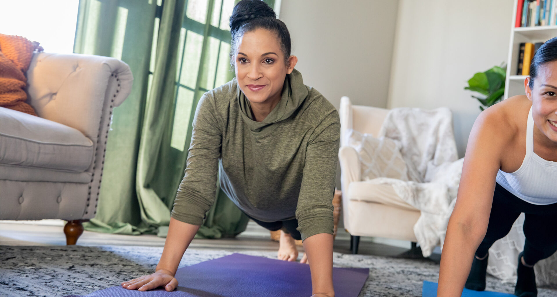 Two women in the high plank position in a living room