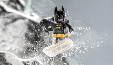 A LEGO Batman minifigure snowboarding down a snowy slope, with snow flying around him and a determined expression on his face.