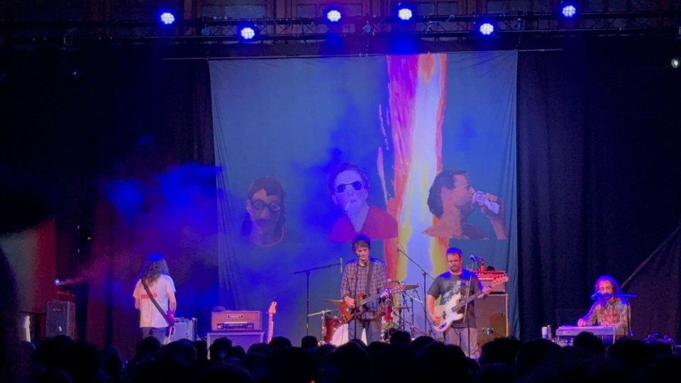 Band performing on stage with a large backdrop.