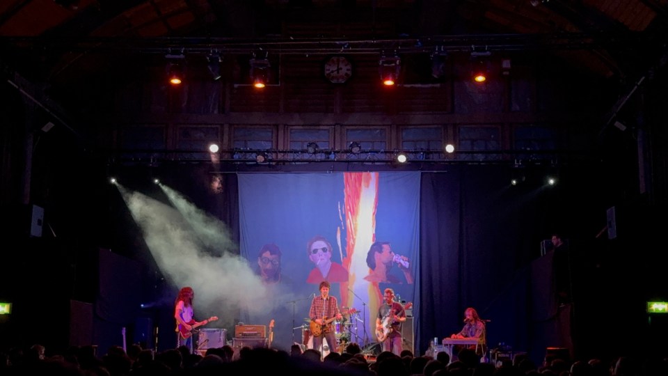 Band performing on stage with a large backdrop.