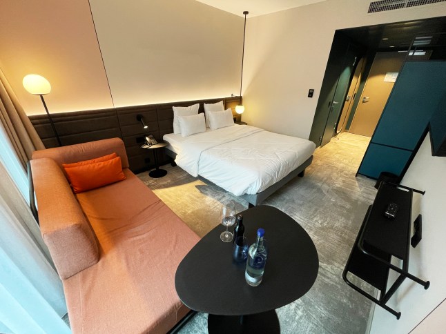 The inside of a bedroom at the Novotel Hamburg. There is an orange sofa bed, a double bed and a black table