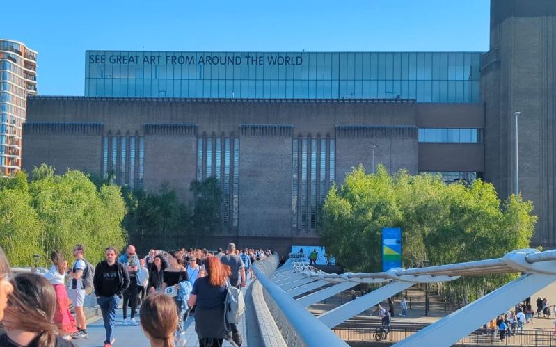 Crowds of people crossing a bridge walking towards the Tate Modern