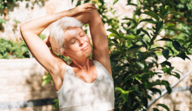 Woman stretches outside with the sun on her face. Her eyes are closed and she looks contented
