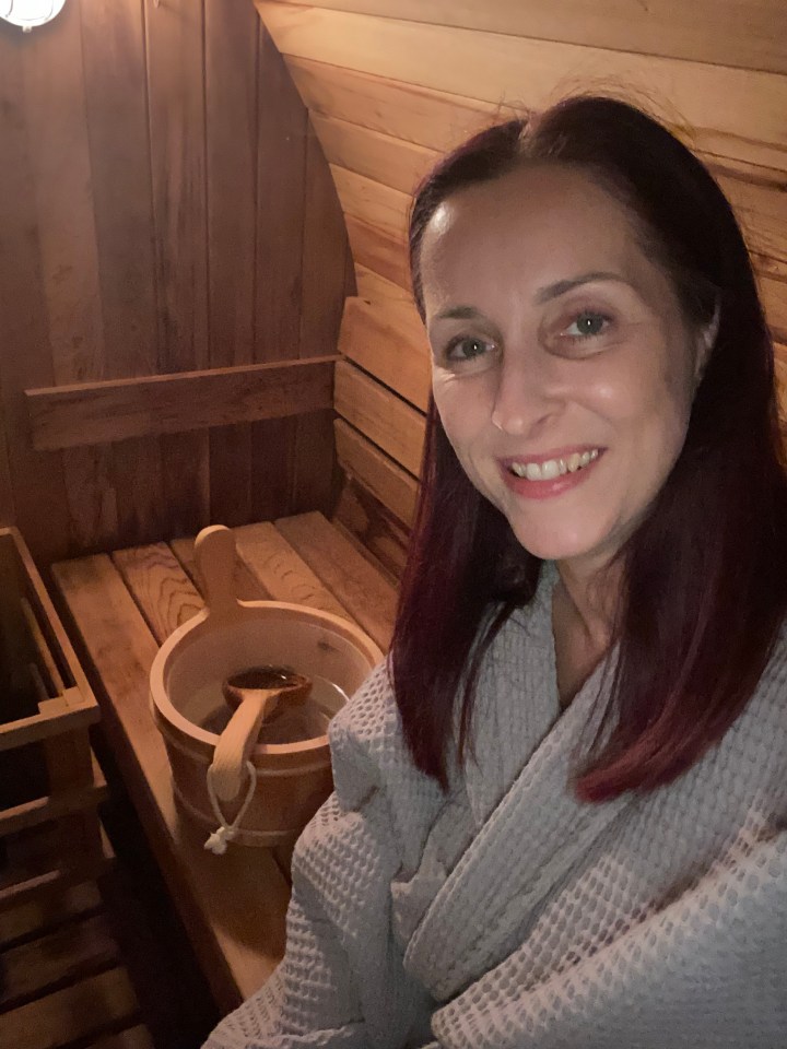 Woman in a gray robe smiling in a wooden sauna.