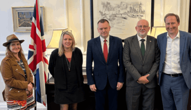 Annabella Coldrick, Naomi Pohl, Nick Thomas-Symonds, Dave Webster and Tom Kiehl smiling in front of a UK flag.