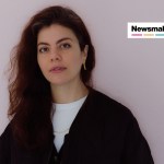 A woman with a black cardigan on looks at the camera. There is a badge in the top right that reads "Newsmakers."