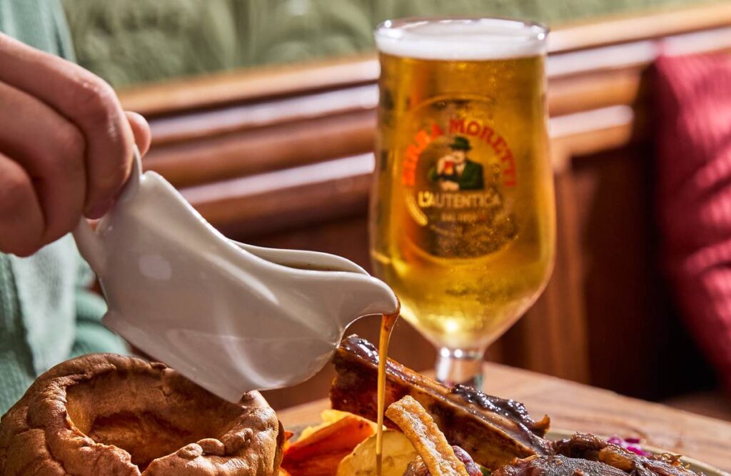 Roast dinner with gravy being poured on it with a pint of Birra Moretti