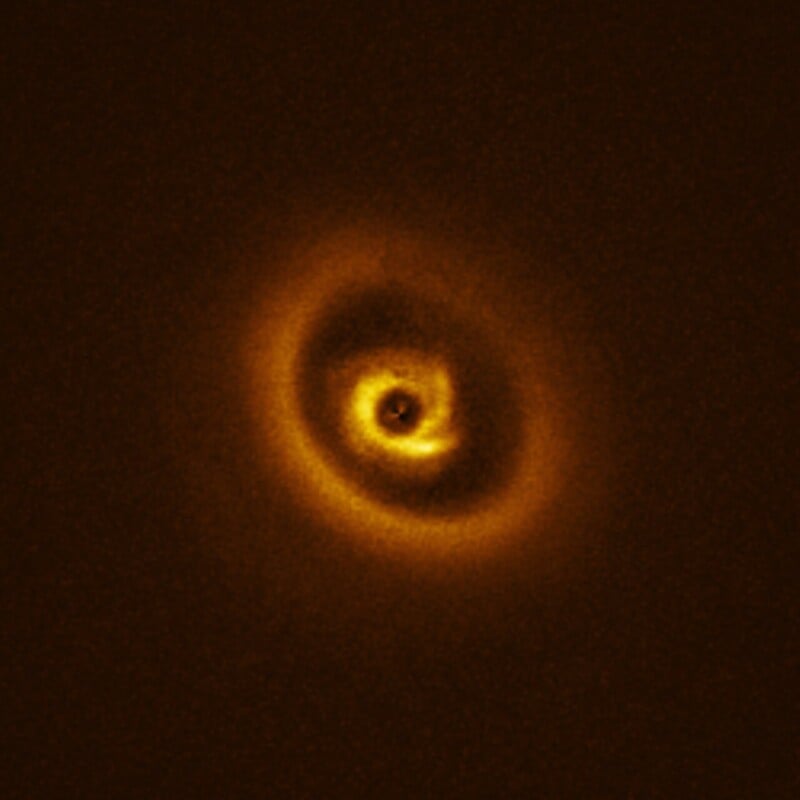 A bright, glowing disk with swirling, spiral patterns and dark gaps, set against a dark background. The image resembles rings of light circling around a central, luminous spot.