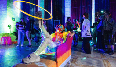 A picture of a person in fluorescent clothes spinning a hoop on their leg with people watching with headphones on