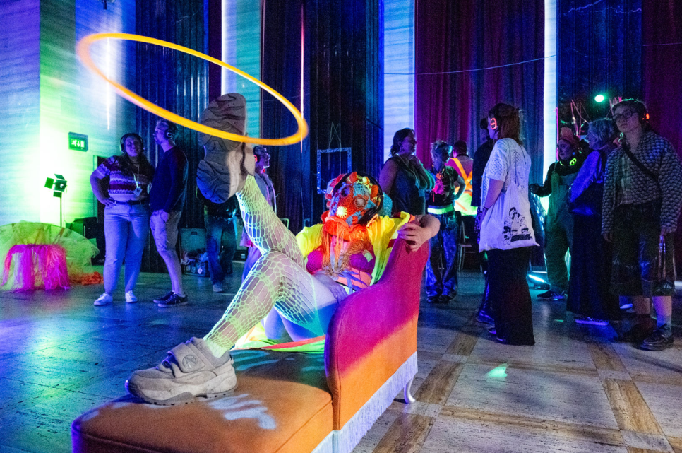 A picture of a person in fluorescent clothes spinning a hoop on their leg with people watching with headphones on