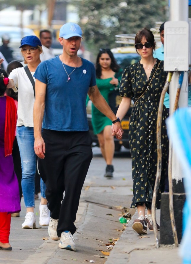 Bandra, INDIA - *PREMIUM-EXCLUSIVE* - Dakota Johnson and Chris Martin were spotted taking a leisurely stroll through Mumbai???s iconic Hanging Gardens, blending seamlessly into the lively surroundings. Walking hand-in-hand through a field of unknowing locals, the couple soaked in the vibrant atmosphere, even pausing to observe local 'Mumbaikers' passionately playing cricket nearby. Chris kept a firm hold on Dakota???s hand, notably free of any rings, as they navigated the bustling area. Dakota looked effortlessly chic in a D??EN Haleigh Dress with a charming Buttercup Bouquet print, retailing for $400, paired with classic Nike Cortez sneakers and a vintage C??line bag. The duo appeared relaxed and in sync, savouring their time in the heart of the city Pictured: Chris Martin, Dakota Johnson BACKGRID USA 21 JANUARY 2025 BYLINE MUST READ: Kaushal/Ajay / BACKGRID USA: +1 310 798 9111 / usasales@backgrid.com UK: +44 208 344 2007 / uksales@backgrid.com *UK Clients - Pictures Containing Children Please Pixelate Face Prior To Publication*