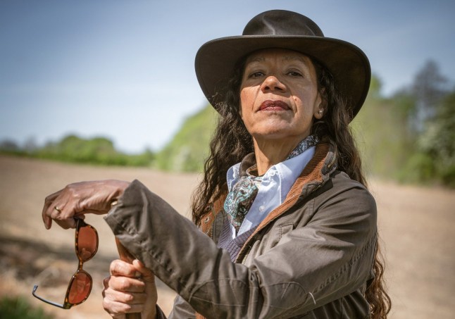 Jaye Griffiths as new farmer Celia in Emmerdale, posing outside a field in a wax jacket and hat.