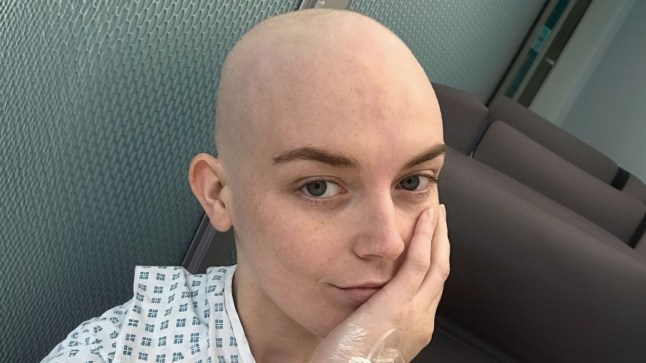 Georgie Swallow in a hospital gown. She has lost her hair in the image and is resting her head against her hand
