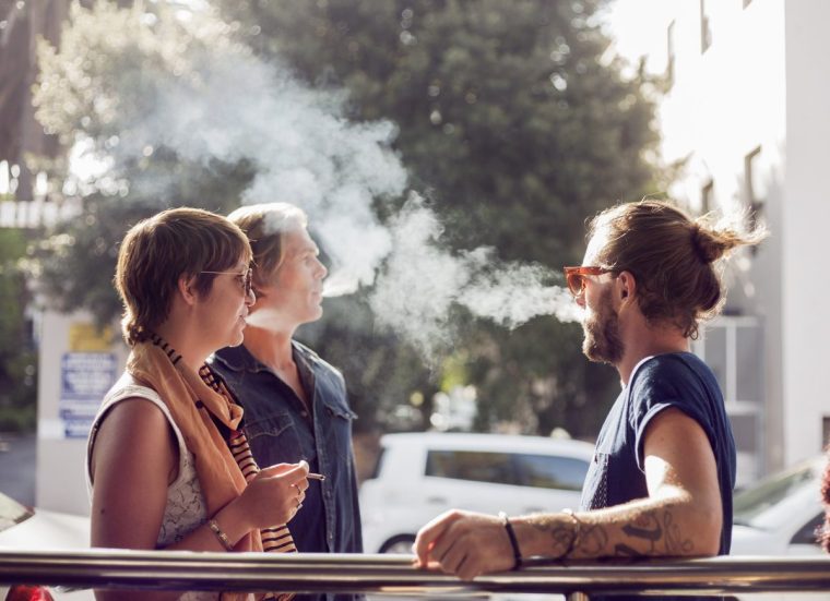 Three people sit outside, smoking