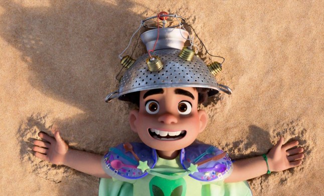 Elio lying on sand with a metal hat on his head in a scene from animated film Elio