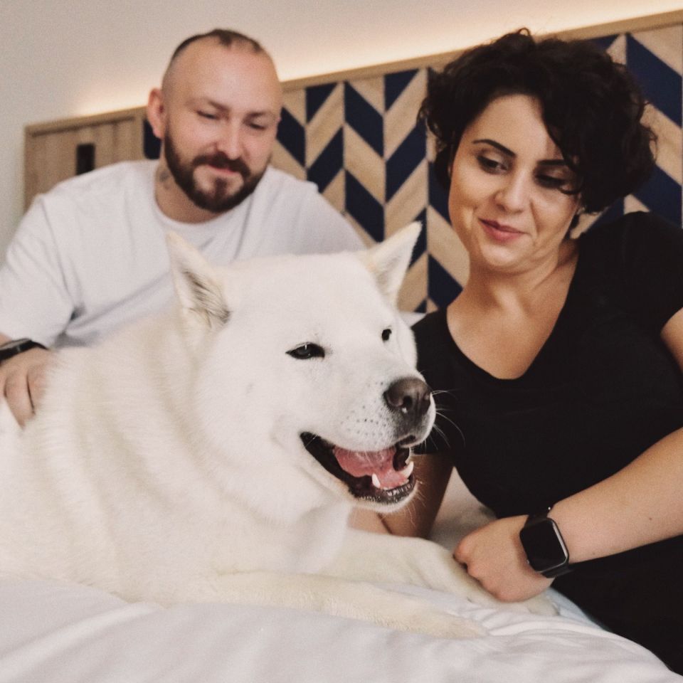 Couple and their white dog on a bed.