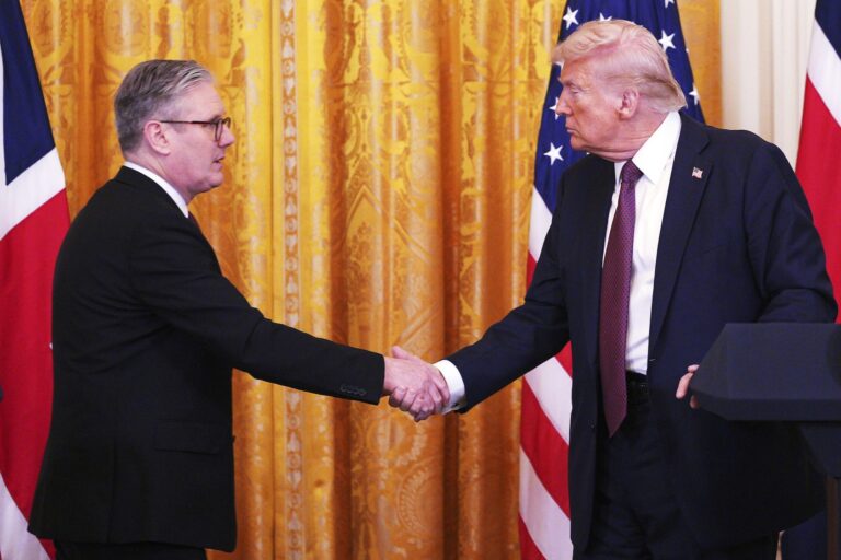 Keir Starmer shaking hands with Donald Trump with a golden curtain and U.S. and U.K. flags in the background.