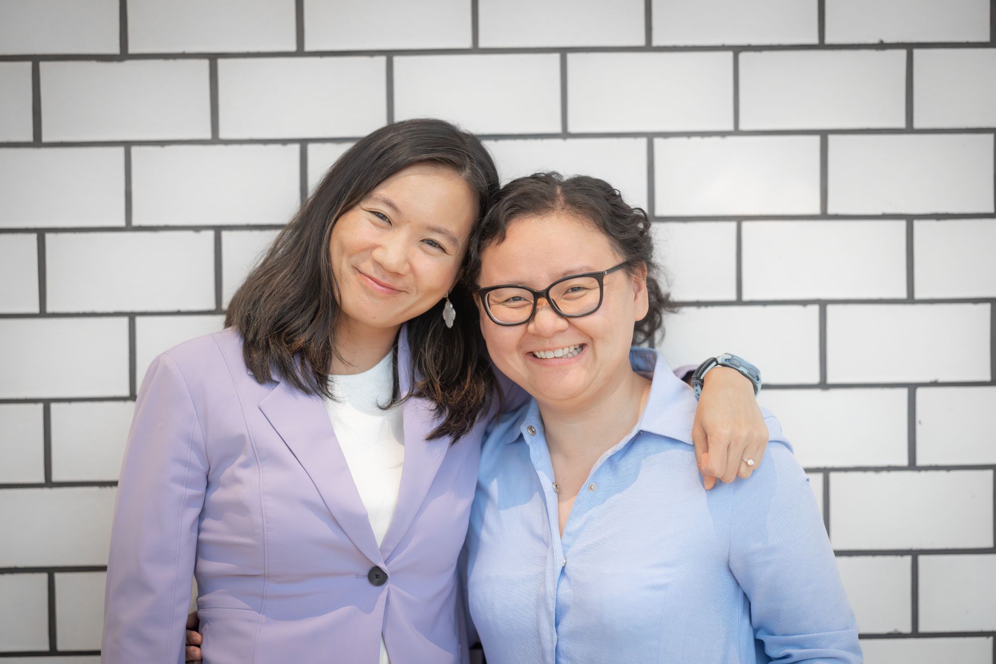 Two women standing in front of a tile wall.