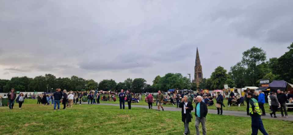 Crowds of people at an outdoor event near food stalls and a church.